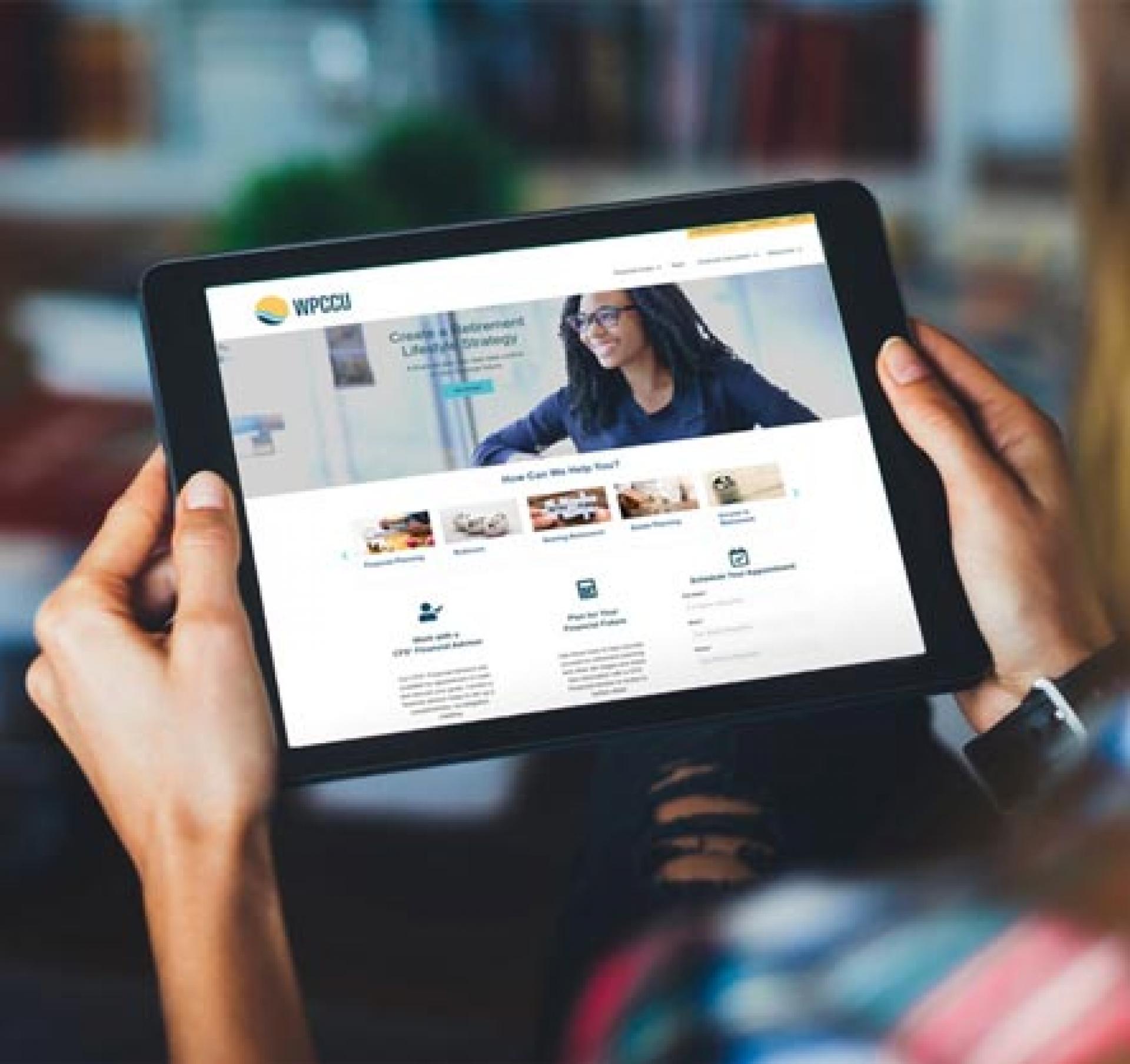 A woman is holding a tablet. The display of the tablet displays a new website. 