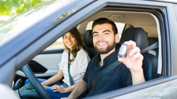 Two people in a car, holding up their car key for a photo. 