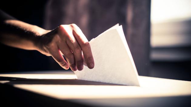 Person dropping a ballot into a ballot box.