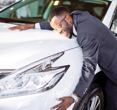 A man is hugging the hood of his new car.