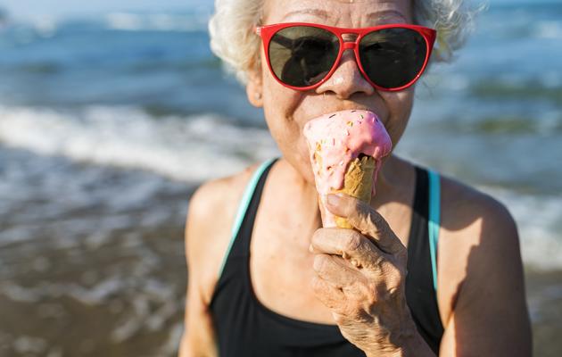 A woman is eating ice cream on the beach.