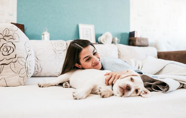 A woman on bed petting and leaning on her dog.