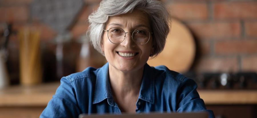 A smiling mature woman with glasses is using her laptop.