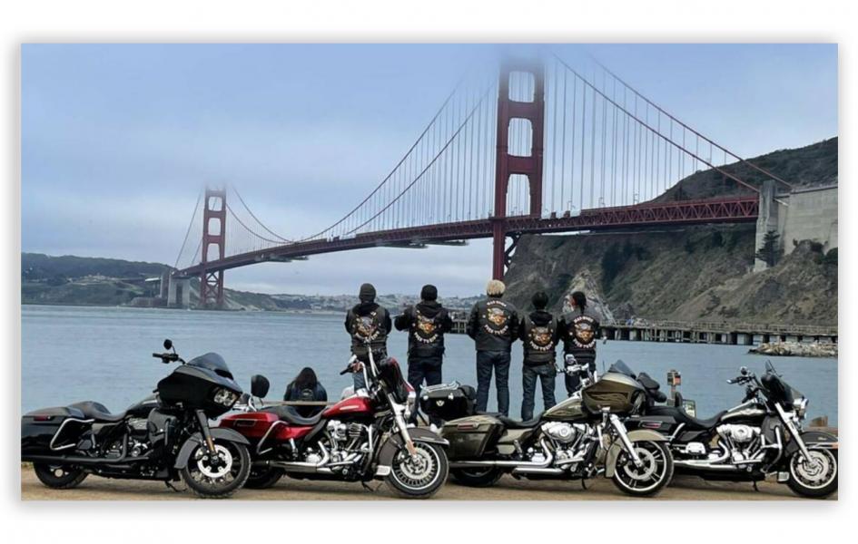 A photo of a group of motorcycle riders standing in front of a bridge.