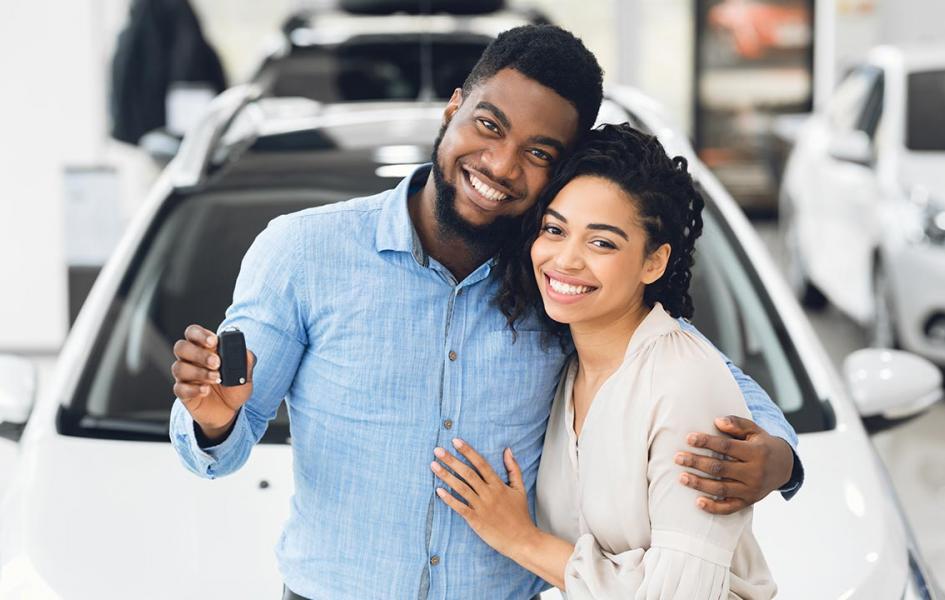 A happy African couple is standing in front of their new car.