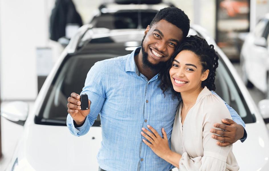 A happy couple is standing in front of their new car.
