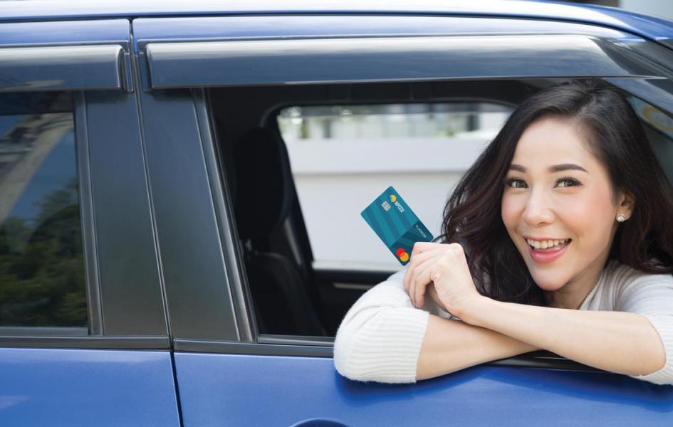 A woman is leaning out of the car window. She's holding WPCCU's Platinum Mastercard.