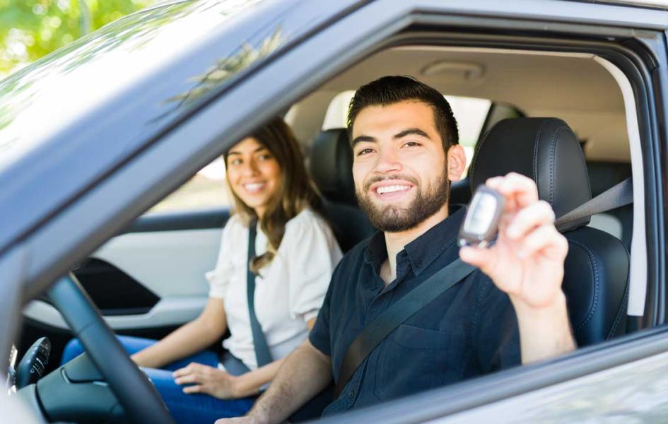 Two people in a car, holding up their car key for a photo. 