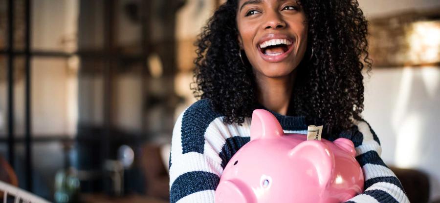 A woman is embracing a big, pink, piggy bank. She is laughing. 