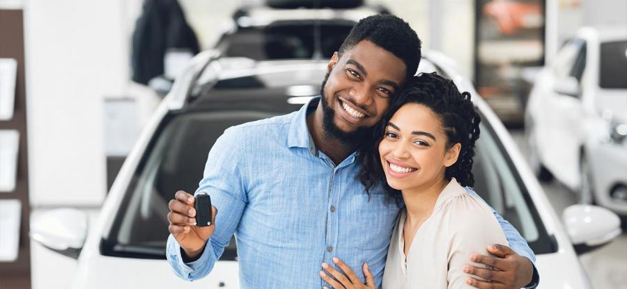 A happy African couple is standing in front of their new car.