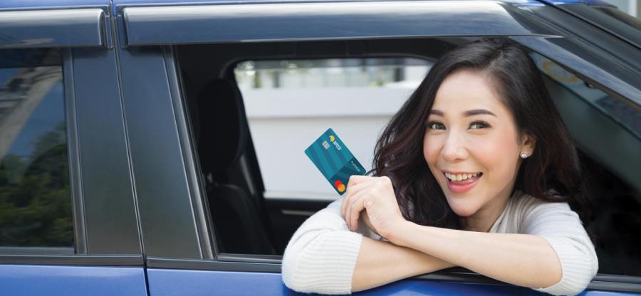 A woman is leaning out of the car window. She's holding WPCCU's Platinum Mastercard.