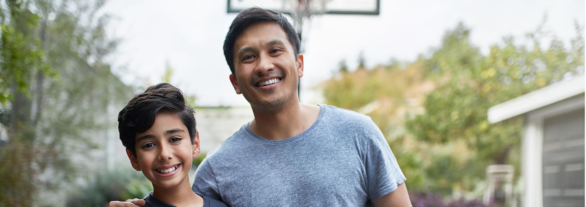 Father and son posing for a photo. The boy is holding a basketball.