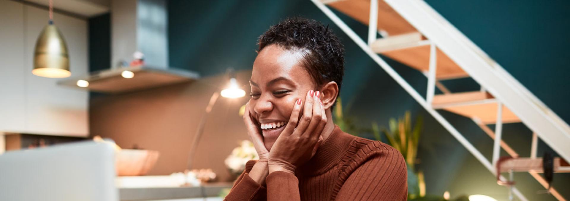 A photo of a woman sitting behind a laptop. She is smiling.