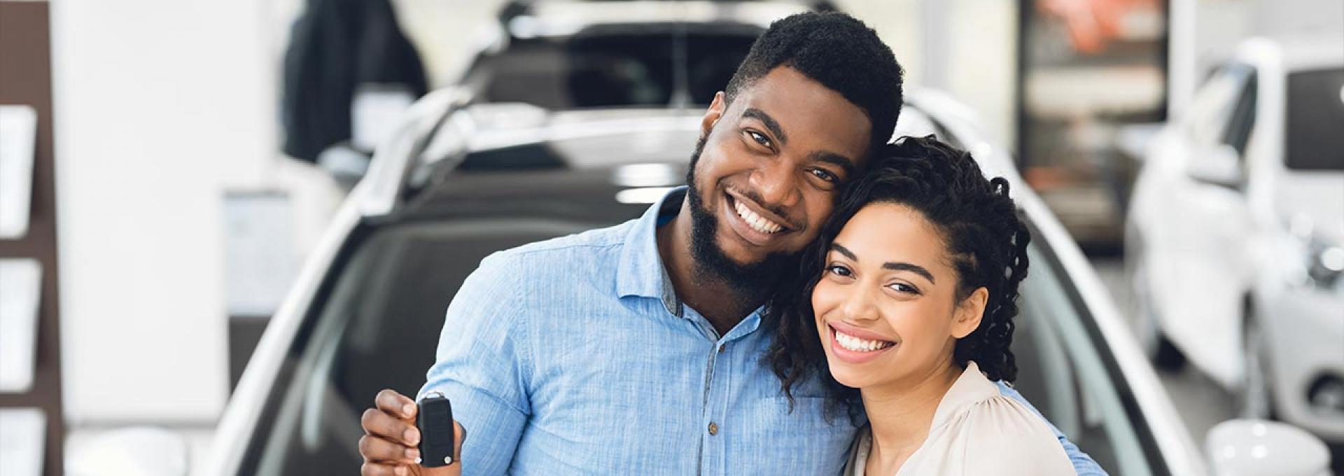 A happy African couple is standing in front of their new car.
