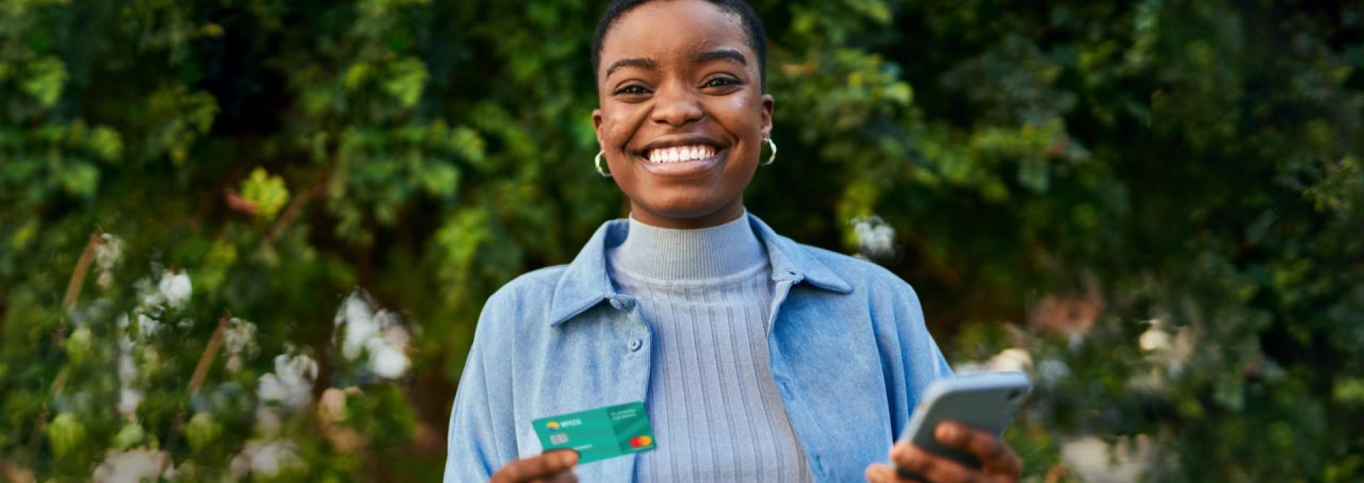 A photo of a joyful African-American woman. She is holding a WPCCU Mastercard in her right hand and a smartphone in her left.