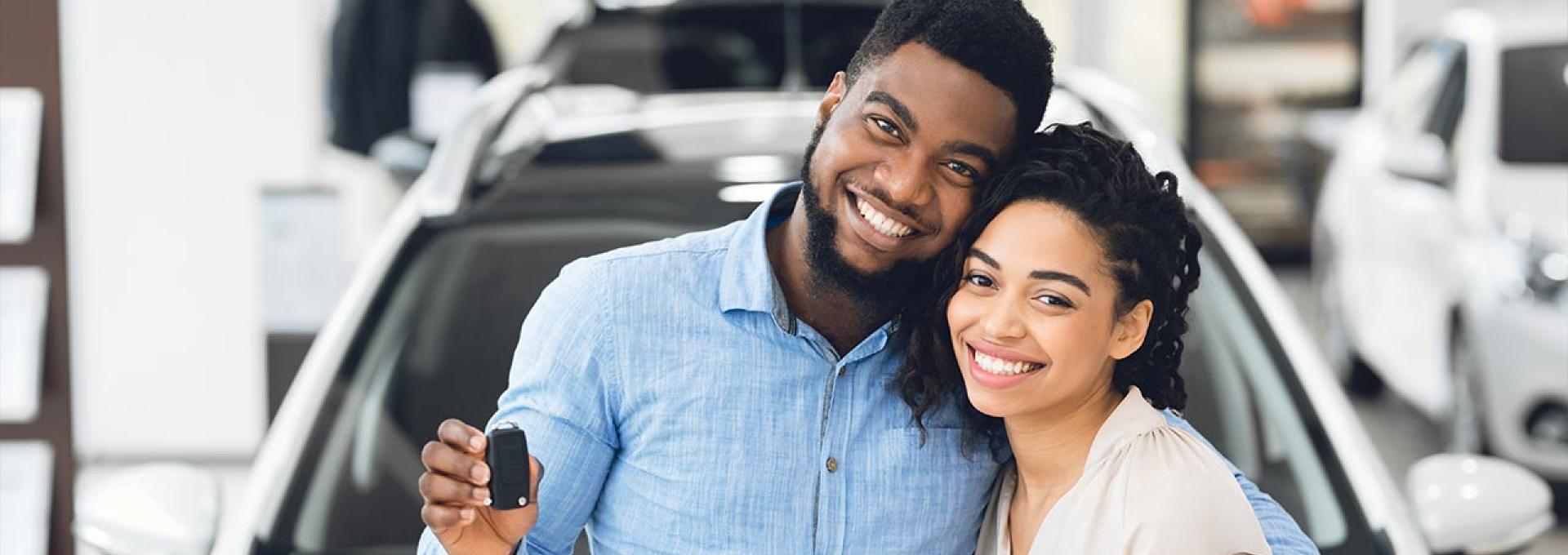 A happy couple is standing in front of their new car.