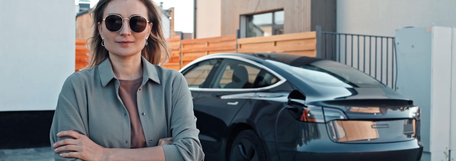 A woman is standing in front of her electric vehicle.