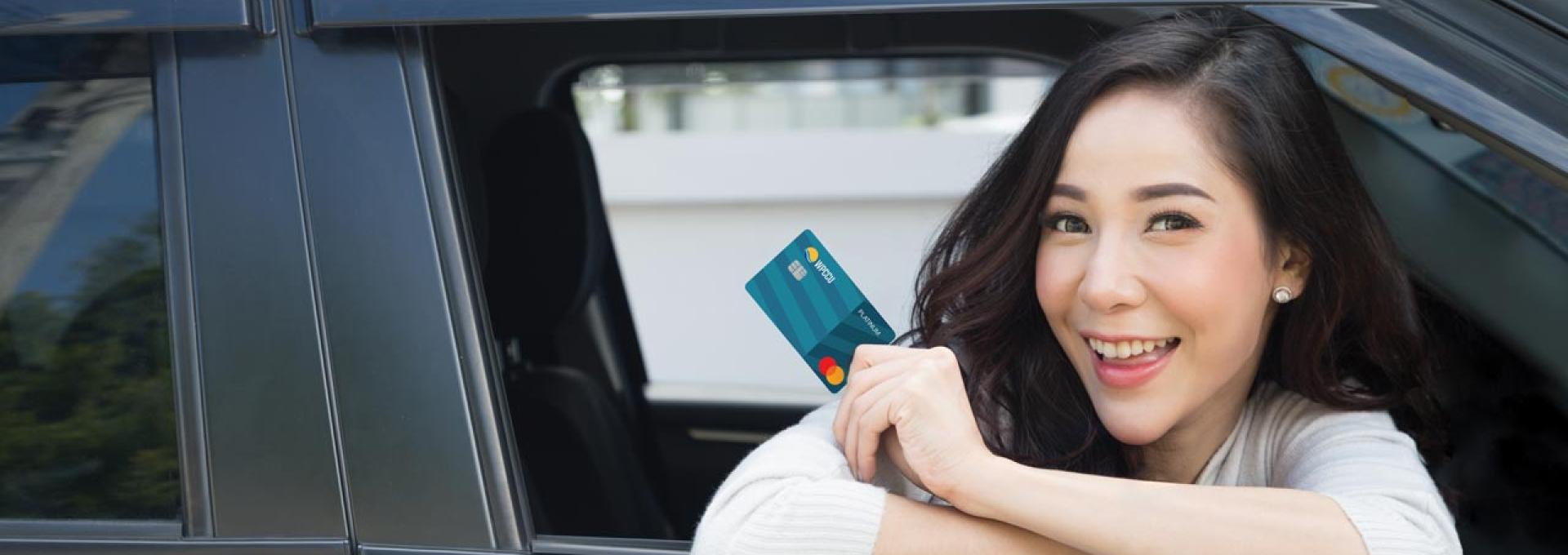 A woman is leaning out of the car window. She's holding WPCCU's Platinum Mastercard.