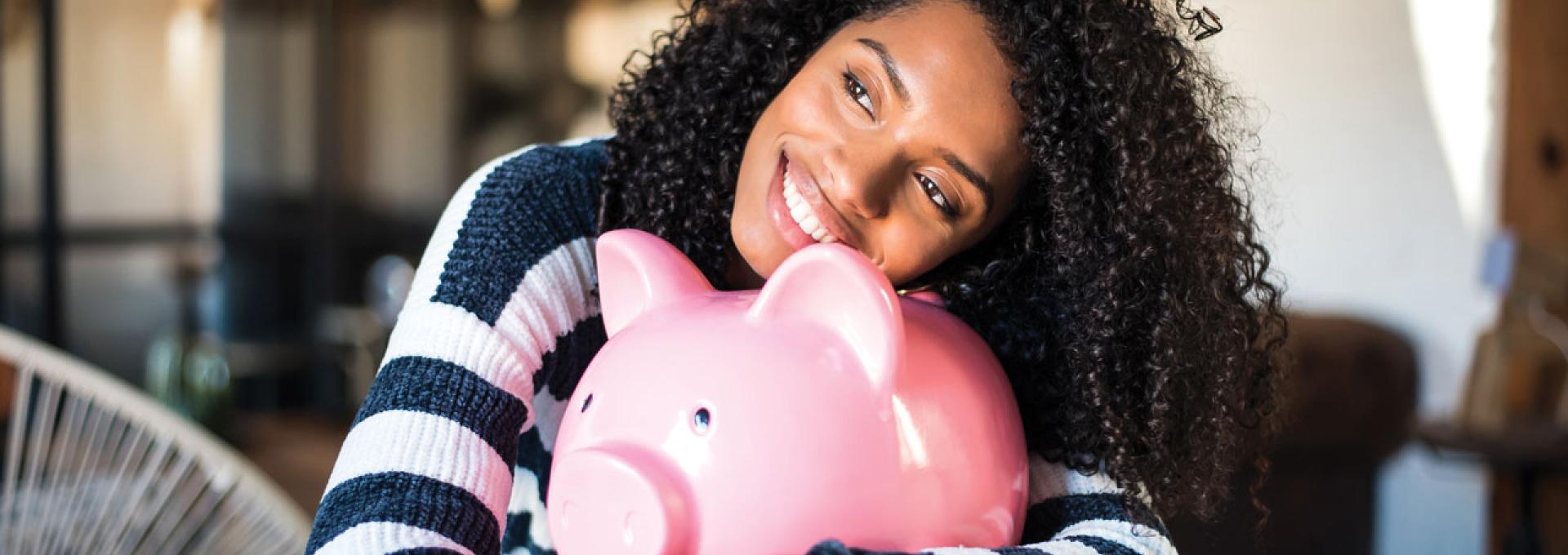 A woman hugging an oversized piggy bank.