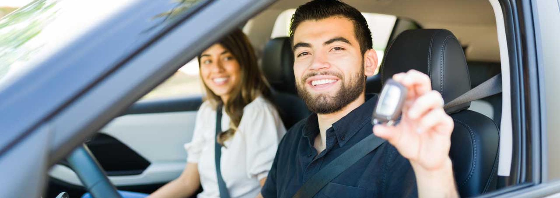 Two people in a car, holding up their car key for a photo. 